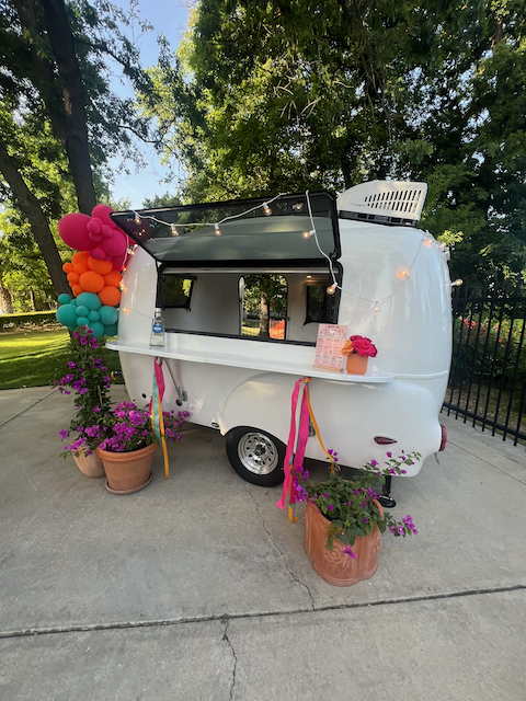 Mobile flower trailer with colorful balloon garland and potted purple arrangements in outdoor setting
